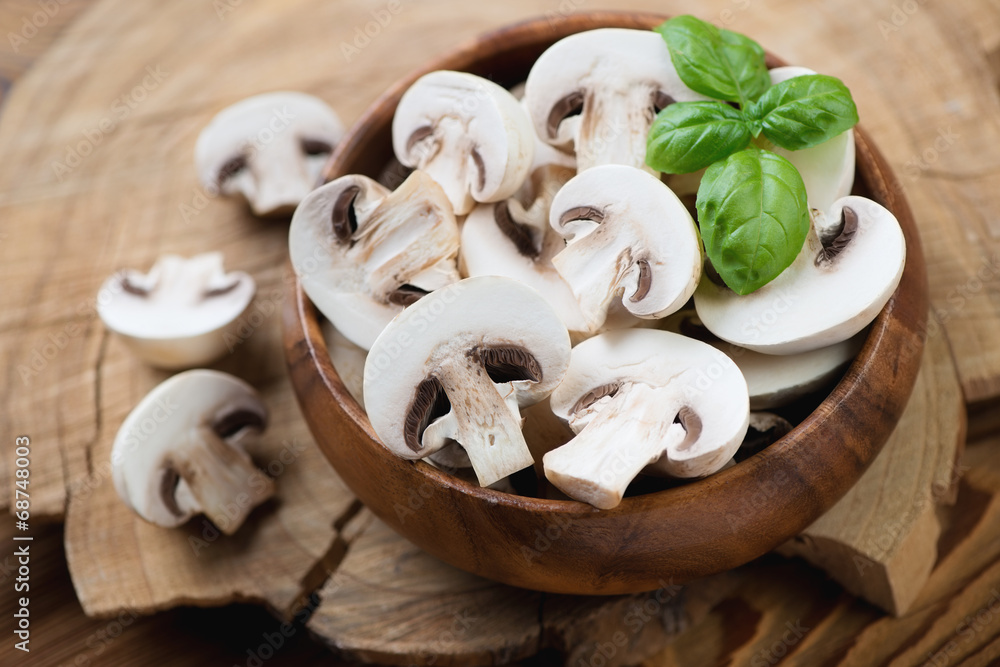 Wooden bowl with fresh champignons and green basil, close-up Wooden bowl with fresh champignons and green basil, close-up