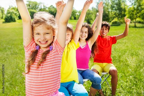 Four kids sitting in row with hands up