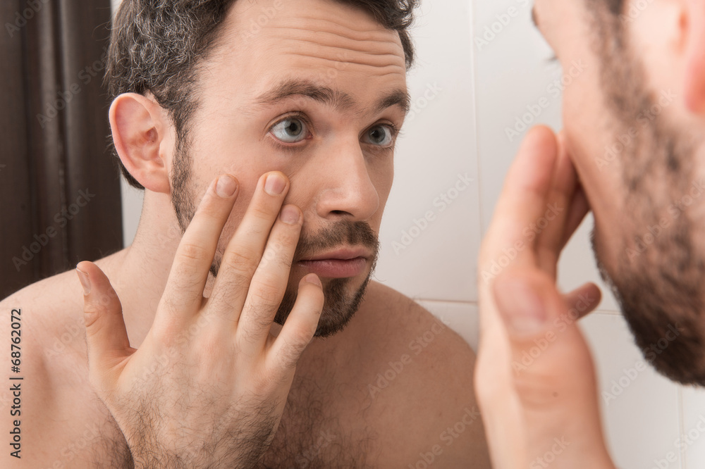 Closeup of young man examining his eye in mirror. Closeup of young man examining his eye in mirror.