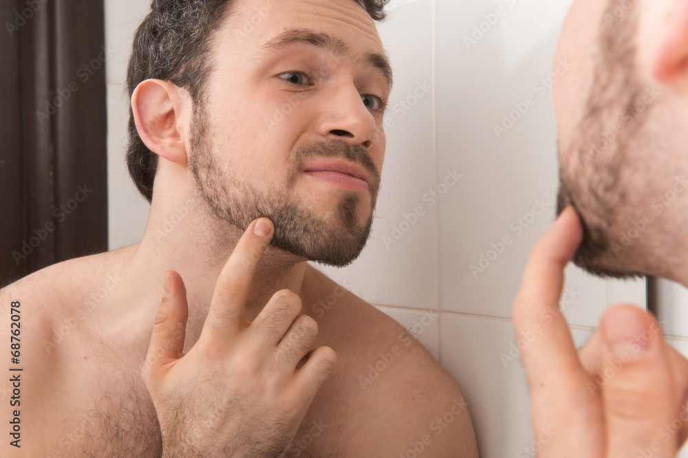 Obraz premium Closeup of young man examining his stubble in mirror.