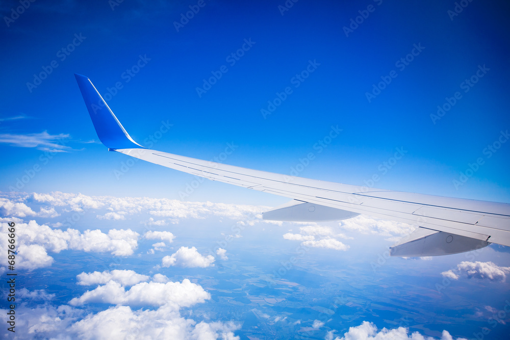 Naklejka premium airplane wing with blue sky and white clouds