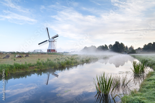 Dutch windmill by river in morning