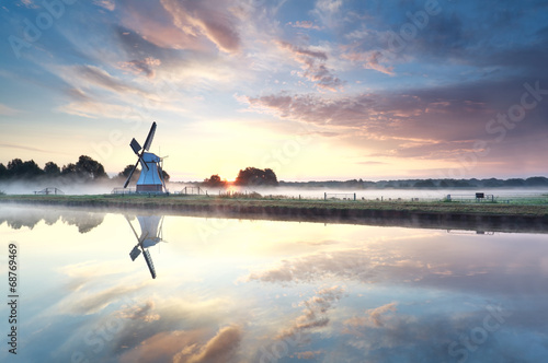 golden sunrise over windmill reflected in river