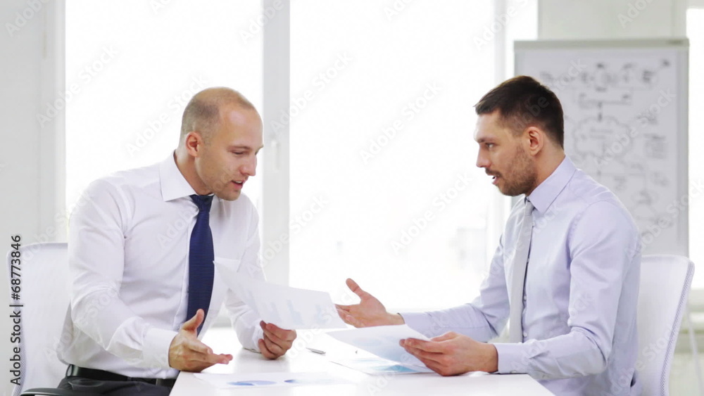 two serious businessmen with charts in office two serious businessmen with charts in office