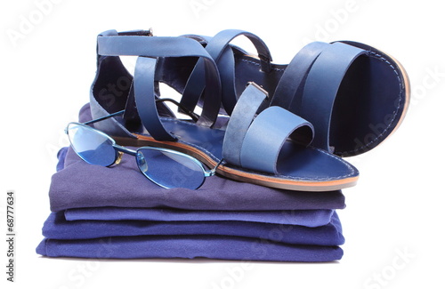 Womanly sandals and sunglasses on pile of blue clothes.