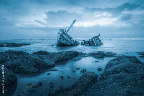 Fotografie Shipwreck or wood ship broken damage on land, coast or beach with sea and sunset background