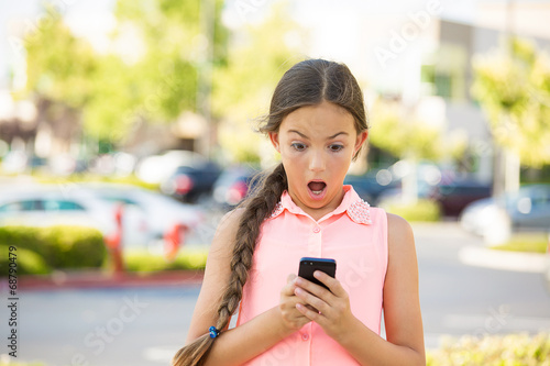 Shocked child texting on mobile, smart phone, outside background