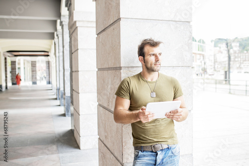 Casual modern man with tablet computer in the street looking awa