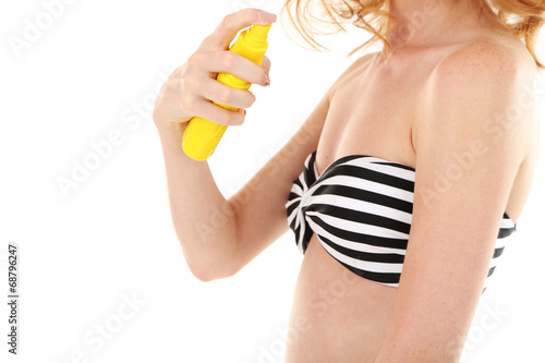 Young woman in swimsuit holding spray tanning isolated on white