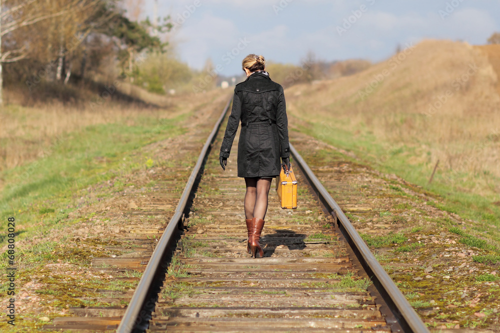 Woman with an old suitcase walking along railway sleepers