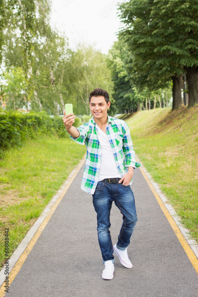 Fototapeta premium Handsome young hipster man taking a selfie in park