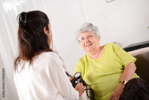 cheerful young doctor taking blood pressure of elderly woman 