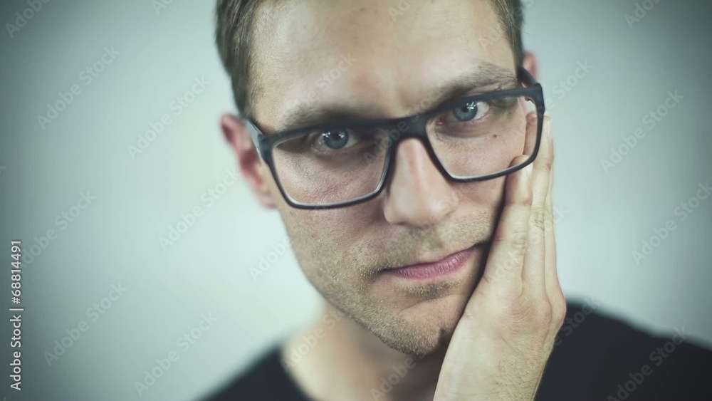 Handsome man in glasses touching his face over grey background Handsome man in glasses touching his face over grey background