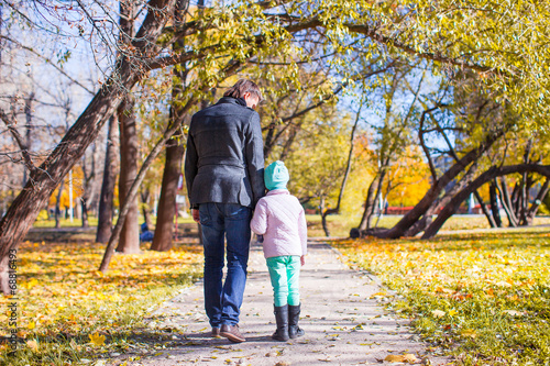 Rear view of young father and little girl walking in autumn park