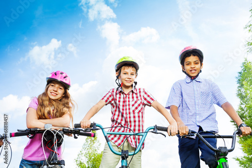 Three kids in helmets hold bike handle-bars