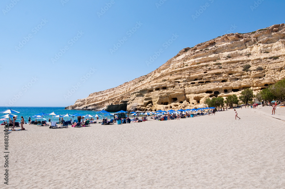 Fototapeta premium Tourists on Matala beach with the caves on Libyan sea, Greece.