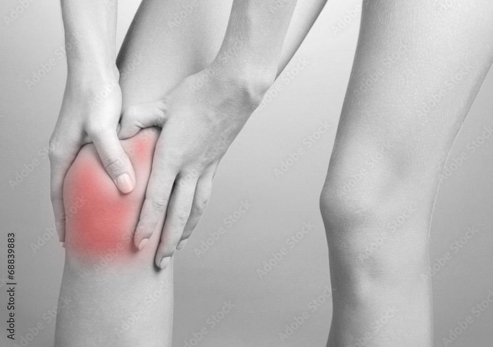 Pain concept. Woman holding sore knee in shades of grey Pain concept. Woman holding sore knee in shades of grey