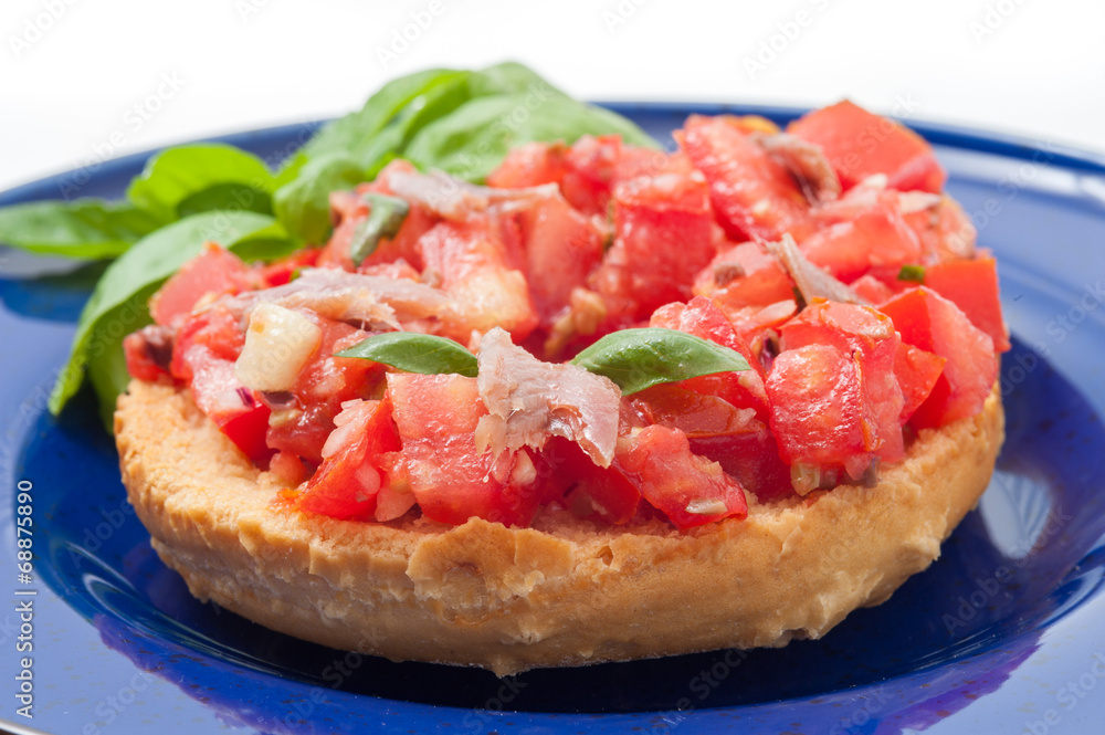 Frisella con pomodori rossi e acciughe su un piatto blu Frisella con pomodori rossi e acciughe su un piatto blu