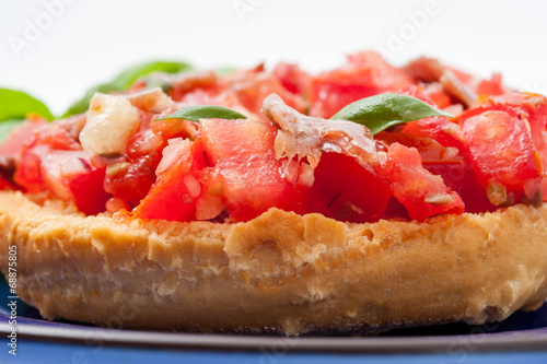 Frisella con pomodori rossi e acciughe su un piatto blu