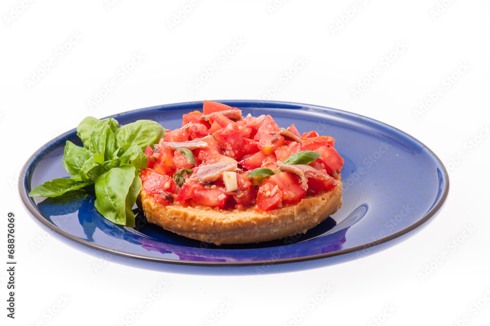 Frisella con pomodori rossi e acciughe su un piatto blu Frisella con pomodori rossi e acciughe su un piatto blu