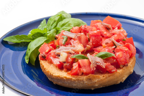 Frisella con pomodori rossi e acciughe su un piatto blu