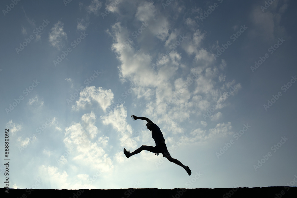 Silhouette of sport man jumping with blue sky and clouds on back