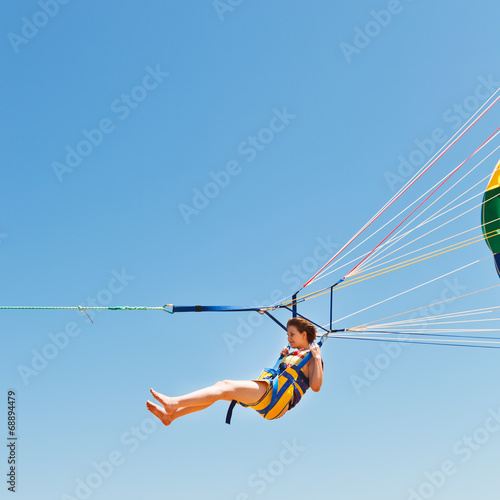 girl parasailing on parachute in blue sky