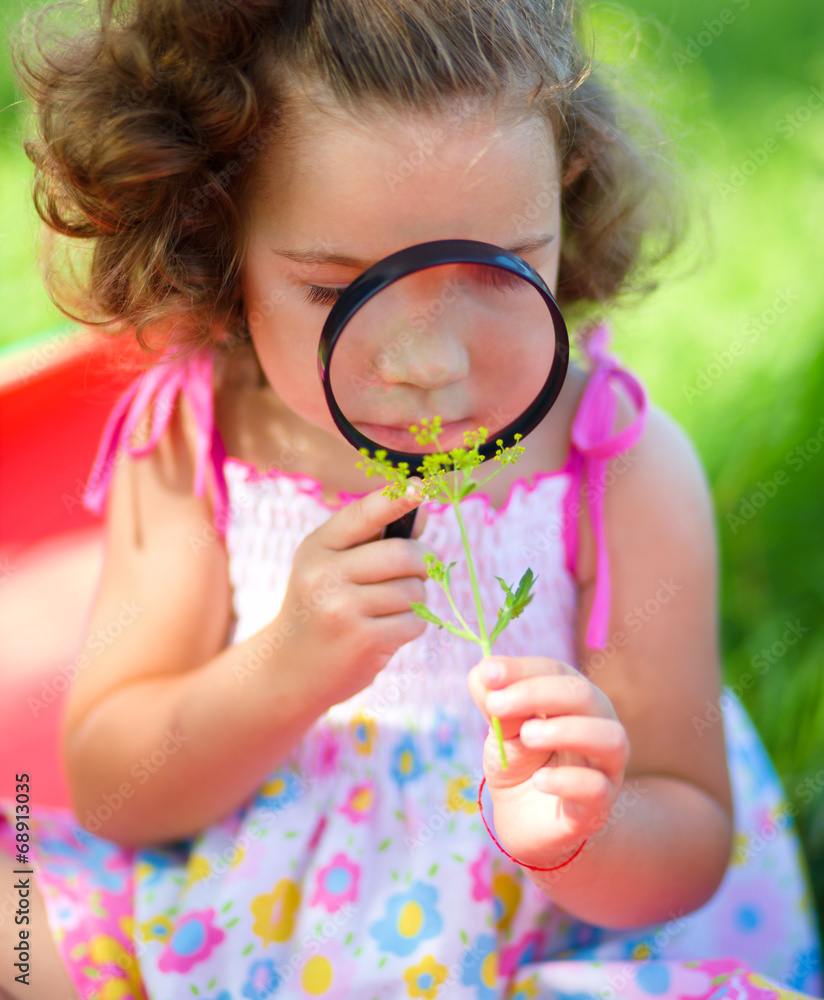 Young girl is looking at flower through magnifier Young girl is looking at flower through magnifier