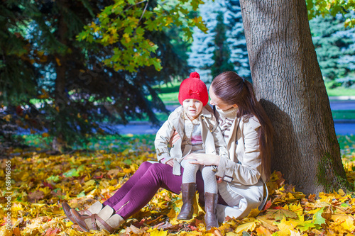 Little girl and young mom in yellow autumn park on sunny day