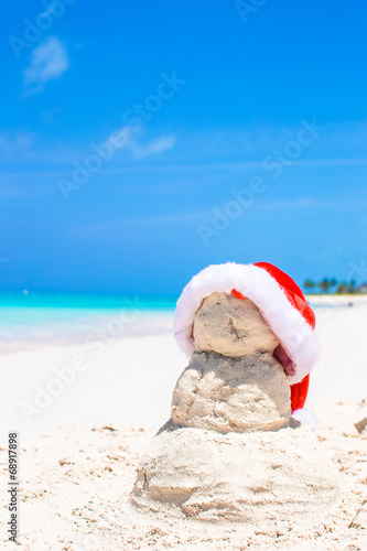 Sandy snowman with red Santa Hat on white Caribbean beach