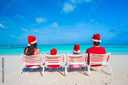 Happy family of four on beach in red Santa hats