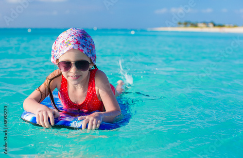 Little adorable girl on a surfboard in the turquoise sea © travnikovstudio