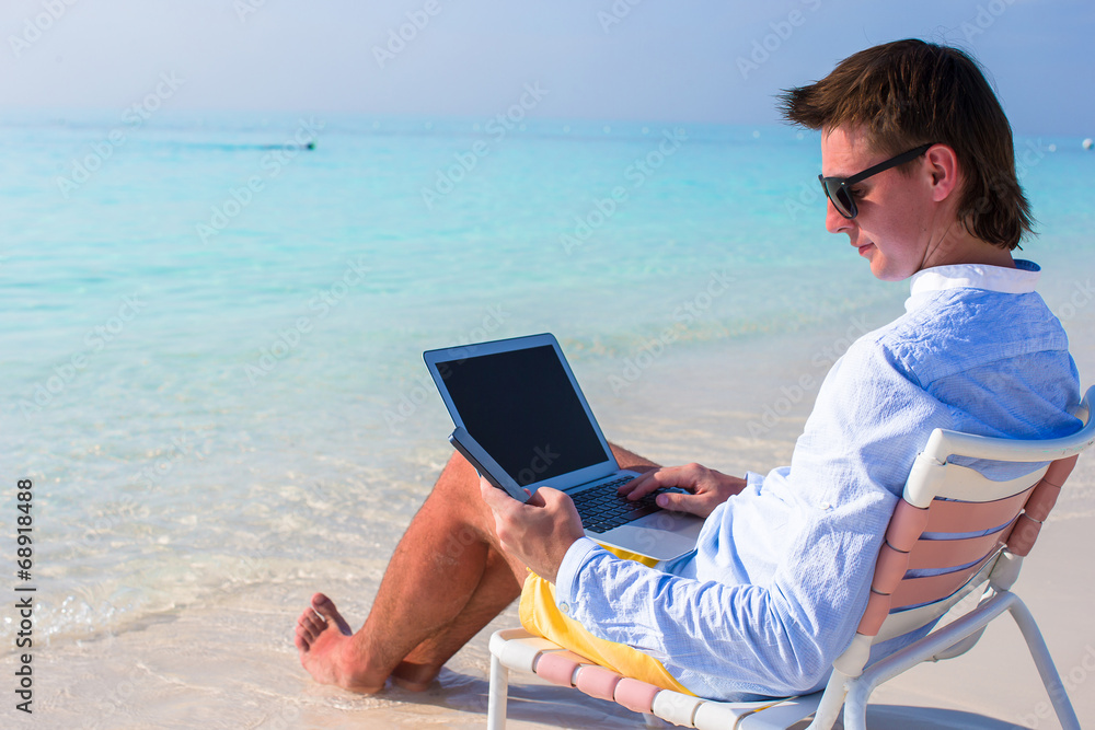 Young businessman using laptop and telephone on tropical beach