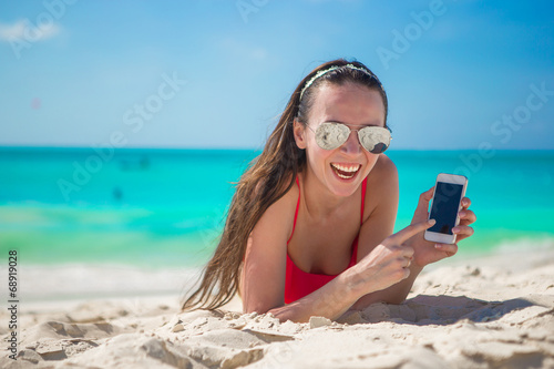 Young woman lying on white sand and talking by cell phone