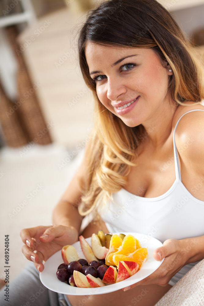 Pregnant woman sitting in her living room and eating fruits