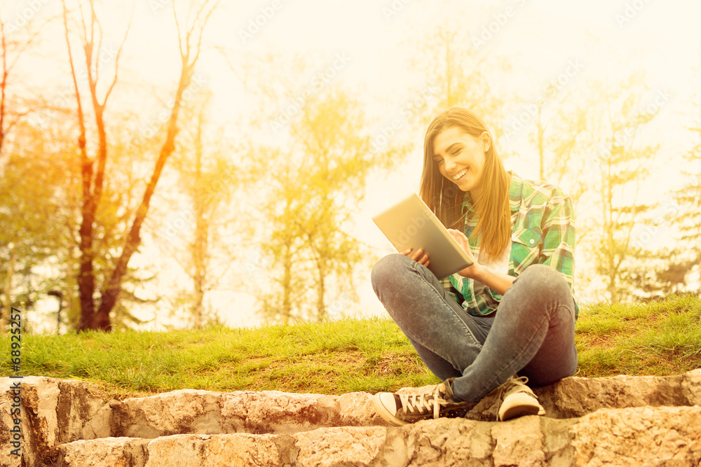 Obraz premium Young woman with tablet sitting in park laughing
