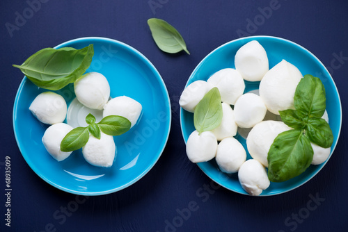 Glass saucers with mozzarella balls and green basil leaves