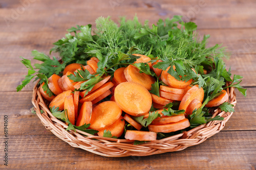 Slices of carrot and parsley in wicker bowl on wooden