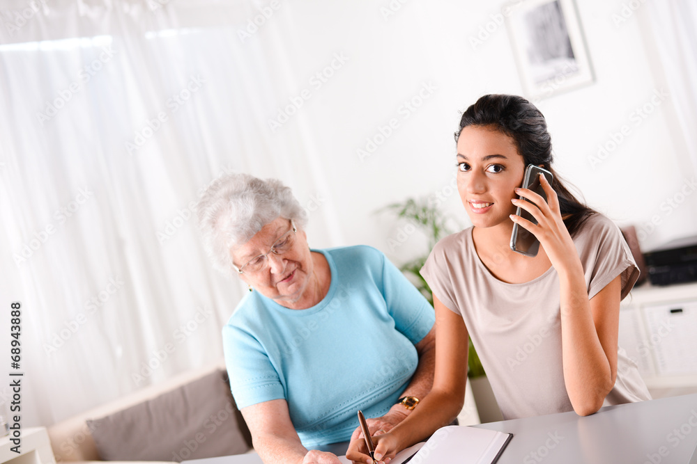 Fototapeta premium young woman helping old person for paperwork and telephone call