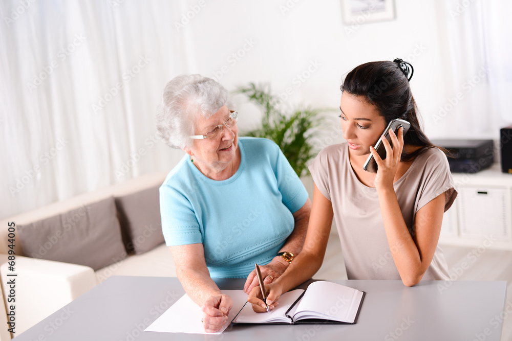 young woman helping old person for paperwork and telephone call young woman helping old person for paperwork and telephone call