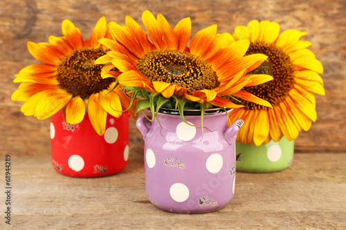 Beautiful sunflowers in cans on table on wooden background