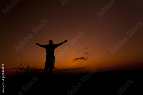 Man worshiping with his hands up in the sunset sky