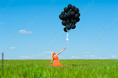 woman in orange dress lets go black balloons