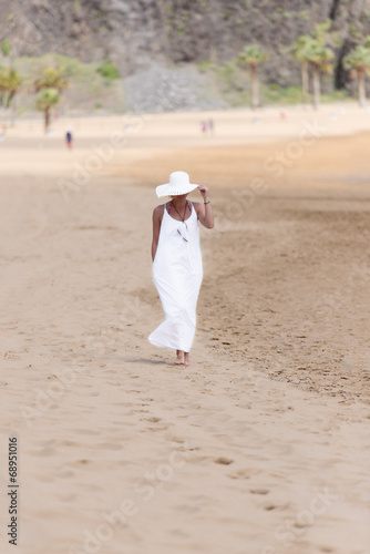 Barefoot girl in white hat and dress walking on a beach