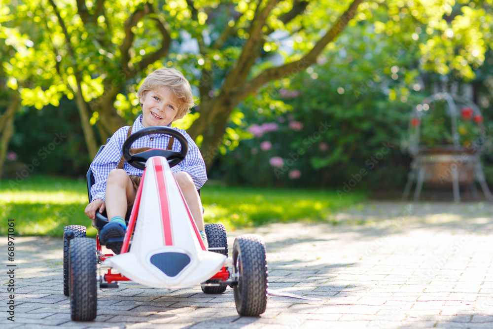 Active little boy driving pedal car in summer garden Active little boy driving pedal car in summer garden