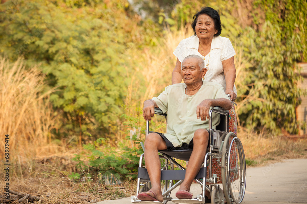 Senior woman pushing her disabled husband on wheelchair Senior woman pushing her disabled husband on wheelchair