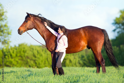 Young beautiful girl walking with a horse in the field
