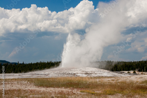 Old Faithful Eruption Against White Clouds