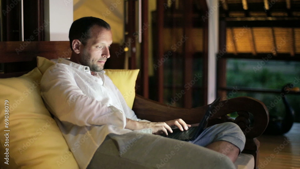 Young man with modern laptop sitting on sofa at night Young man with modern laptop sitting on sofa at night
