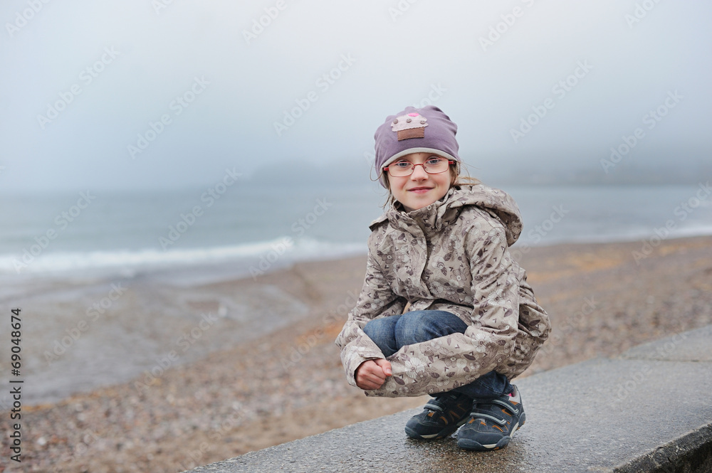 Adorable kid girl on the beach in rainy day.